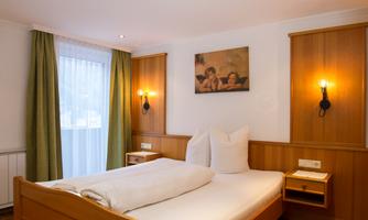 A cozy room with a double bed and wooden paneling. Large windows bring in plenty of light, and an art photo hangs on the wall.