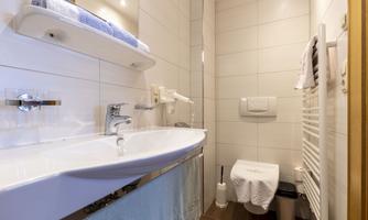 A modern bathroom with a large sink and bright tiles. Towels and a towel holder are also available.