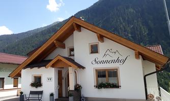 A cozy house with the inscription "Sonnenhof" in the mountains. The surroundings are green and the sun is shining.