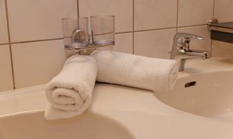 A bathroom sink with two clean towels and glasses. The faucet shines and the walls are brightly tiled.