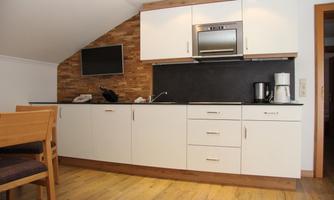A modern kitchen with wooden floors and a combination of white and dark surfaces. There is a refrigerator, a coffee machine, and a stove.