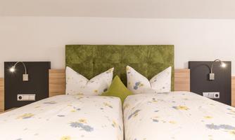 A cozy bedroom with two beds and floral bedding. Green accents and modern nightstands give the room an elegant look.
