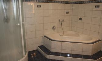 A bathroom with a bathtub and a shower. The walls are tiled and the floor has a dark covering.
