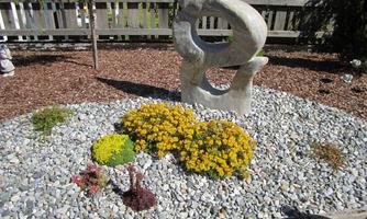 A decorative garden with a stone sculpture and colorful flowers. The area is designed with gravel and bark mulch.
