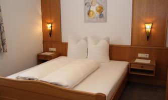 A modern bedroom with a double bed and cozy pillows. The walls are painted in warm tones and there are decorative wall lamps.