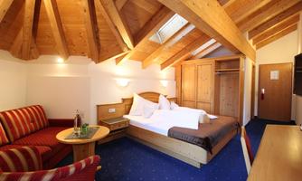 A cozy hotel room with a wooden ceiling, a large bed, and a seating area. The decor is modern and inviting.