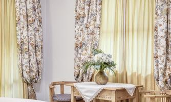 A cozy room with a wooden table and chairs. The curtains are floral and the atmosphere feels bright and inviting.