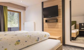 A cozy hotel room with a large double bed and wooden paneling. The room features a television and a large window overlooking the outdoors.