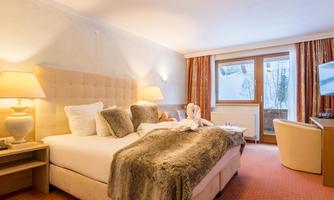 A stylish bedroom with a large bed and cozy pillows. In front of a window overlooking a snowy landscape stands a television and a table.