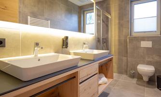 A modern bathroom with double sinks and wooden shelves. The walls are in warm gray tones, and a large shower creates a pleasant atmosphere.