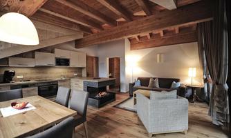 A modern apartment with a wooden ceiling and cozy interior. The space features an open kitchen, a dining area, and a sitting corner.