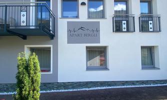 A modern building named "Apart Bergli". It has large windows, balconies, and a well-maintained garden area.