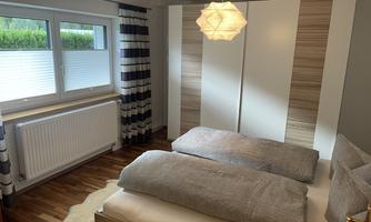 A modern bedroom with two single beds and a stylish light fixture. Large windows provide plenty of natural light and a pleasant atmosphere.