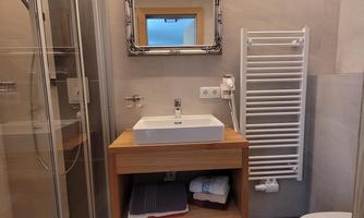 A modern bathroom with a shower, a sink, and a mirror. The walls are light, and the floor is dark tiled.