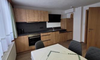 A modern kitchen with wooden cabinets and a dining table. It is bright and spacious, with a window that lets in natural light.