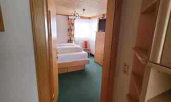 A cozy bedroom with a double bed and bright furniture. The floor is covered with green carpet and there is plenty of storage space.
