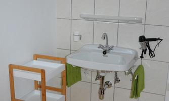 A simple bathroom with a sink and a mirror. The room features a towel holder and a small wooden cabinet.