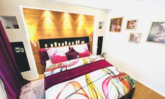 A cozy bedroom with a colorful bed set and a wooden wall. The decorative pictures and soft lighting create an inviting atmosphere.