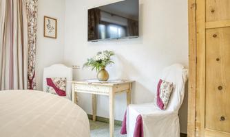 A cozy room with a table and two chairs. A TV hangs on the wall, and a vase with flowers sits on the table.