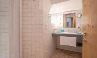 A modern bathroom with tiled walls and a large mirror. On the vanity, there are grooming products and fresh towels.