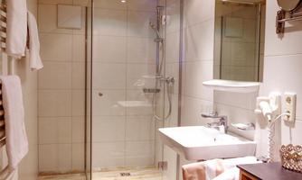 A modern bathroom with a glass shower and a white sink. The floor has a wood look, and there are some towels as well as a decorative mattress.
