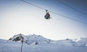 A cable car glides over a snow-covered landscape. In the background, high mountains can be seen.