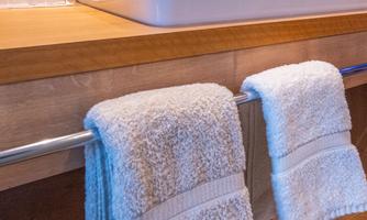 A modern bathroom with a white ceramic sink and wooden elements. Two white towels hang on a towel rack.