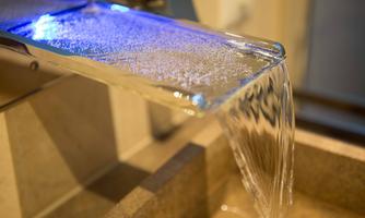A modern faucet with a blue light flow. The water flows clear and evenly into a basin.