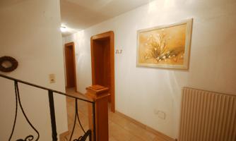 A bright hallway with two doors and a painting on the wall. The floor is tiled and there is a visible radiator.