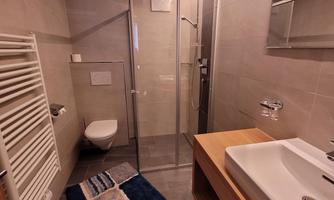 A modern bathroom with a shower, a sink, and a rug. The walls are brightly tiled, and there is a towel radiator.