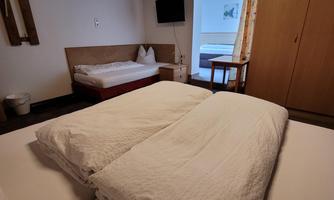 A simple bedroom with two beds and a wooden ceiling. There is a table, a television, and a wardrobe in the room.