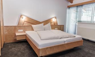 A modern bedroom with a double bed and wood paneling. The room is bright and welcoming with a large window front.