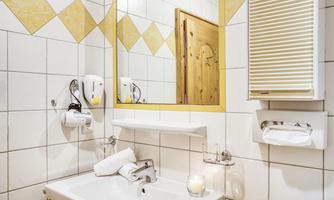 A modern bathroom with white tiles and yellow accents. A mirror above the sink and towels are neatly arranged.