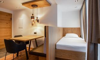 A modern room with a single bed and a dining table. The warm wood tones create a cozy atmosphere.