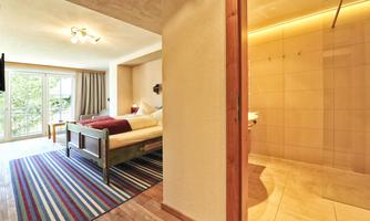 A modern room with a bed and colorful carpet. In the background, a bathroom with a shower is visible.