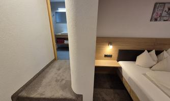 A modern furnished room with a bed and pillows. On the left, a staircase leads to another room.