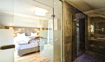 A modern room with a large bed and an elegant shower. The glass door separates the sleeping area from the bathroom.