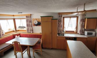 A cozy kitchen with a dining area and a large table. The walls are light-colored, and there are windows that let in plenty of daylight.