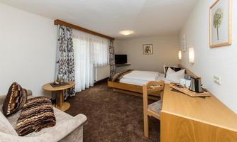 A cozy room with a double bed, a table, and a sofa. Large windows provide plenty of daylight and a pleasant atmosphere.