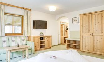 A cozy hotel room with wooden furniture, a television, and a window. The decor feels bright and inviting.