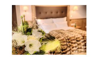 A stylishly furnished bedroom with a cozy bed and soft lighting. In the foreground is a beautiful bouquet.