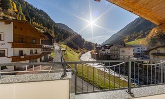 A picturesque mountain landscape with houses by the riverbank. The sun shines over the mountains and nature is brightly colored.
