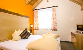 A cozy room with a double bed and bright colors. There is a window with curtains and a television next to a wardrobe.