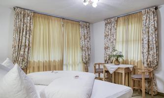 A cozy room with comfortable beds and bright curtains. At the window, there is a small table with chairs and fresh flowers.