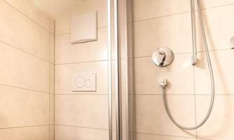 A modern bathroom with a separate shower and a toilet. The walls are light tiled and the floor is black.