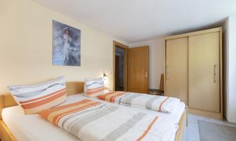 A cozy bedroom with a double bed and colorful cushions. The room has a wardrobe and a picture on the wall.