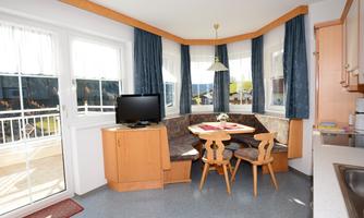 A cozy corner with a dining table and a television.  
Large windows provide plenty of daylight and offer a view of the surroundings.