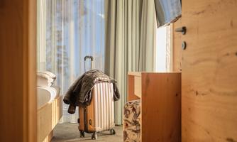 A modern hotel room with a suitcase and a window that lets in daylight. The furniture is simple and elegant.