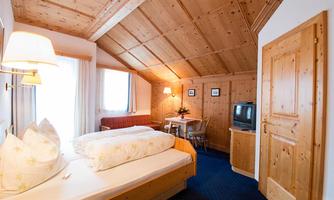A cozy room with wooden paneling and sloping roofs. There is a bed, a table with chairs, and a small seating area.
