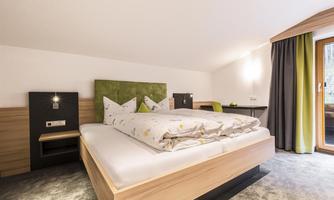 A bright and modern bedroom with a large bed and a green headboard. The room has large windows and a cozy atmosphere.